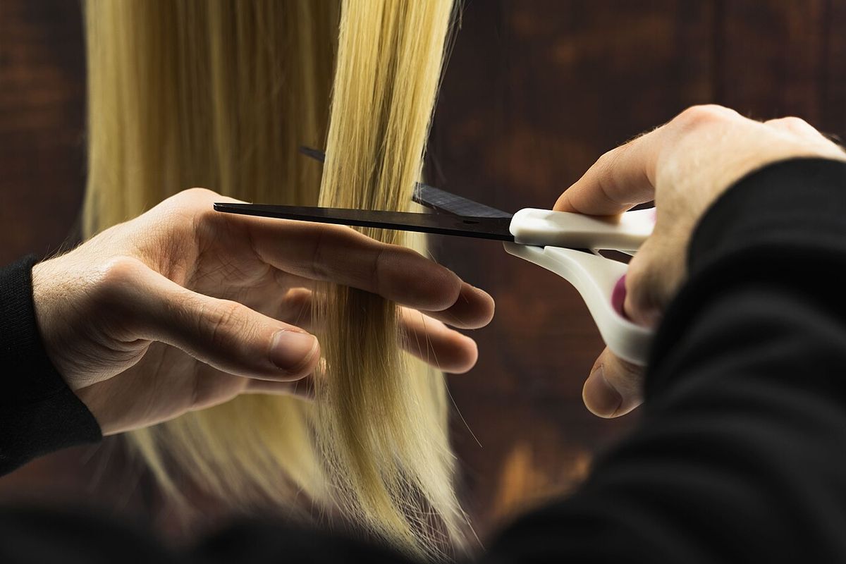A stylist's hands cutting a section of long blonde hair with scissors
