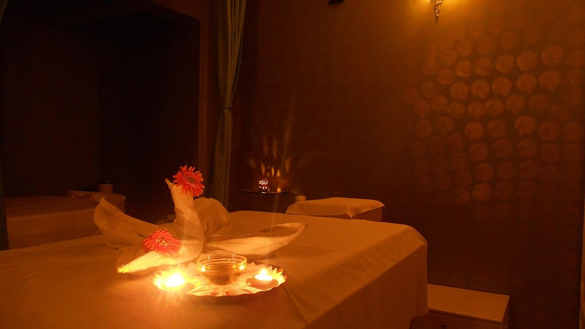 A candlelit massage room with a towel folded into a swan, orange flowers and a glass bowl between two tea lights