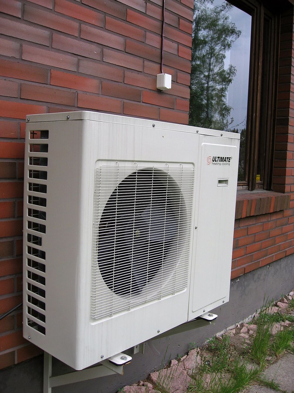 An outdoor heat pump unit mounted beside a brick wall