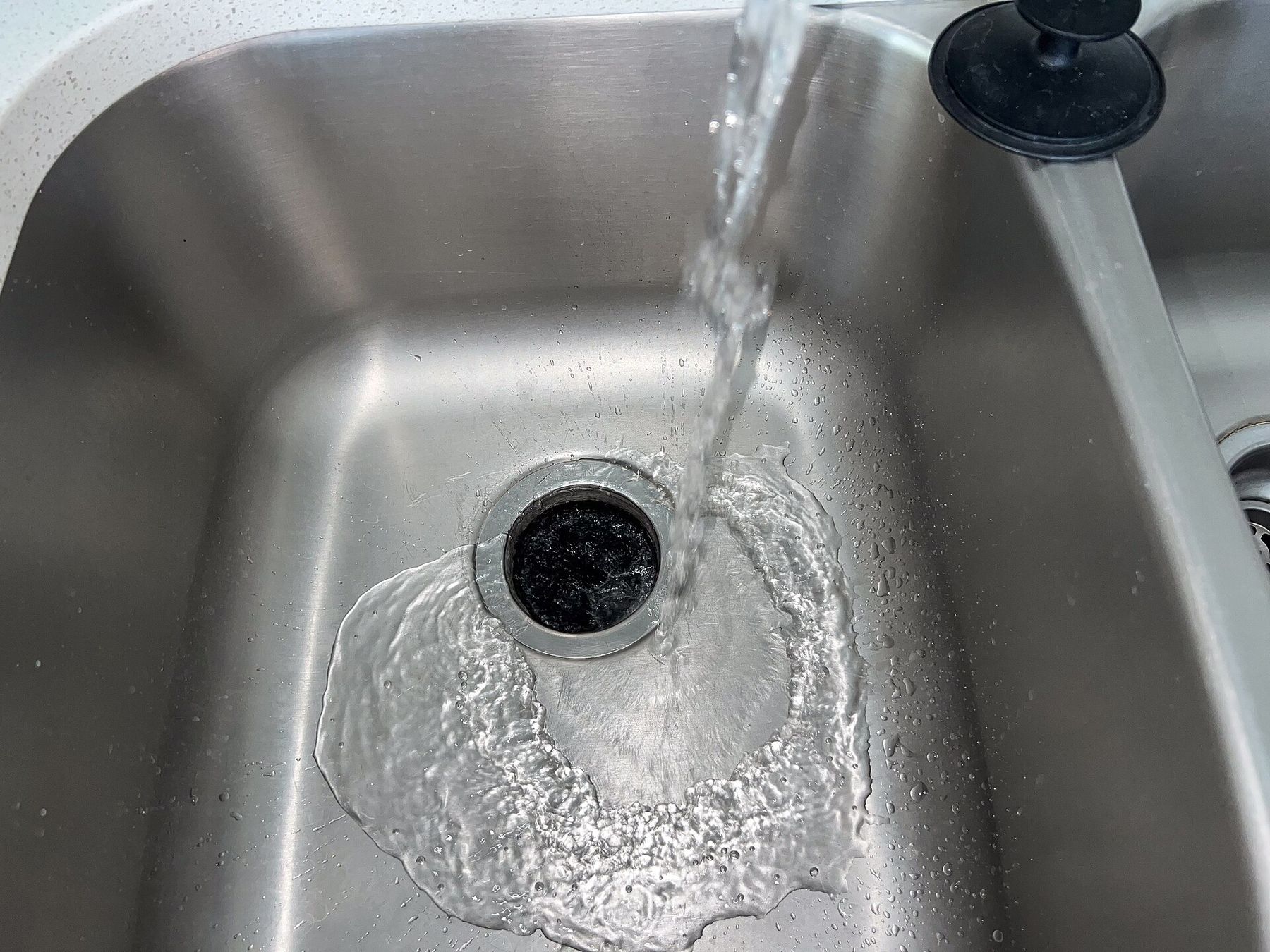 Water running from a tap into a stainless steel sink and down the drain