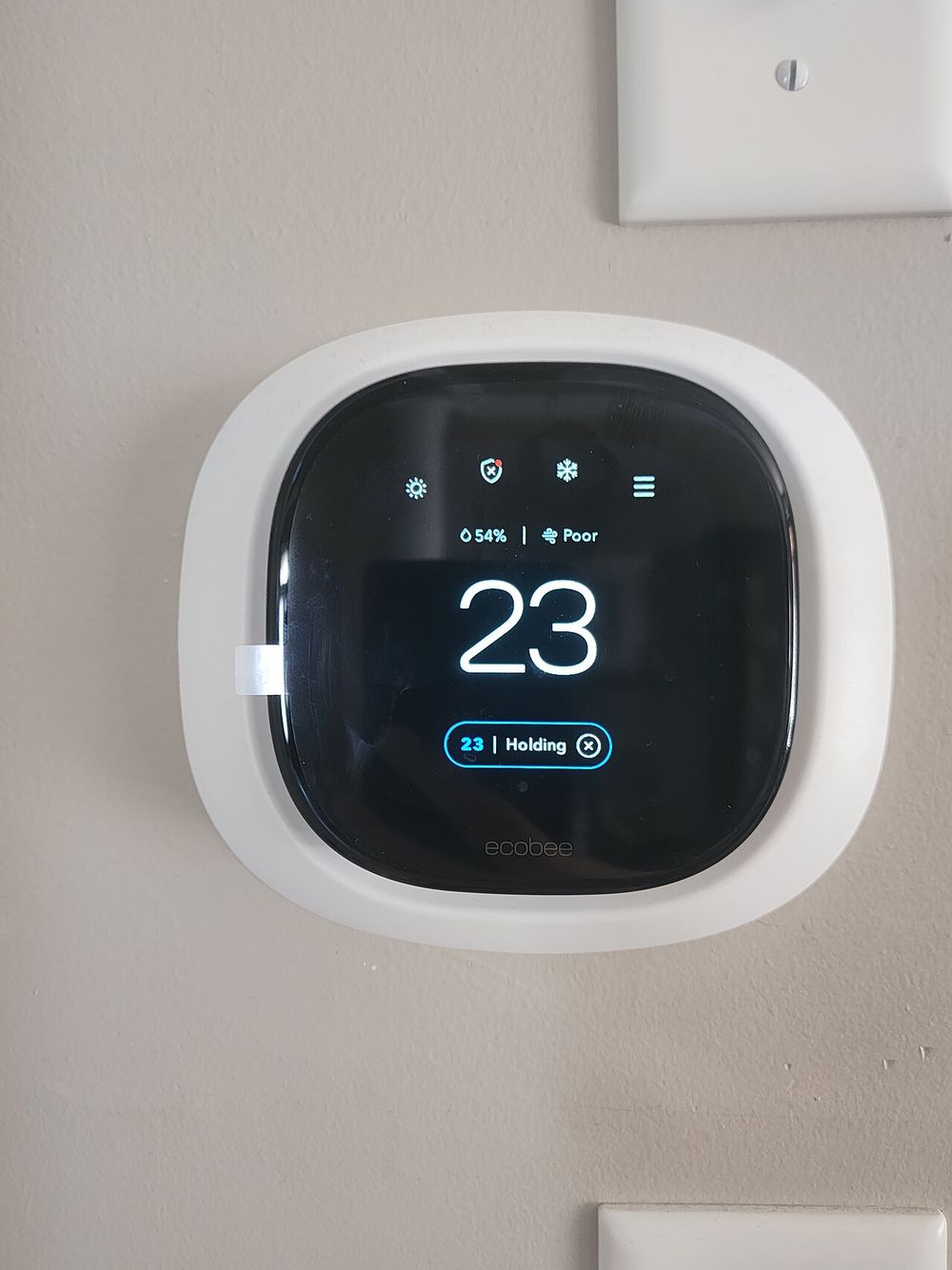 A smart thermostat showing 23 degrees on a wall
