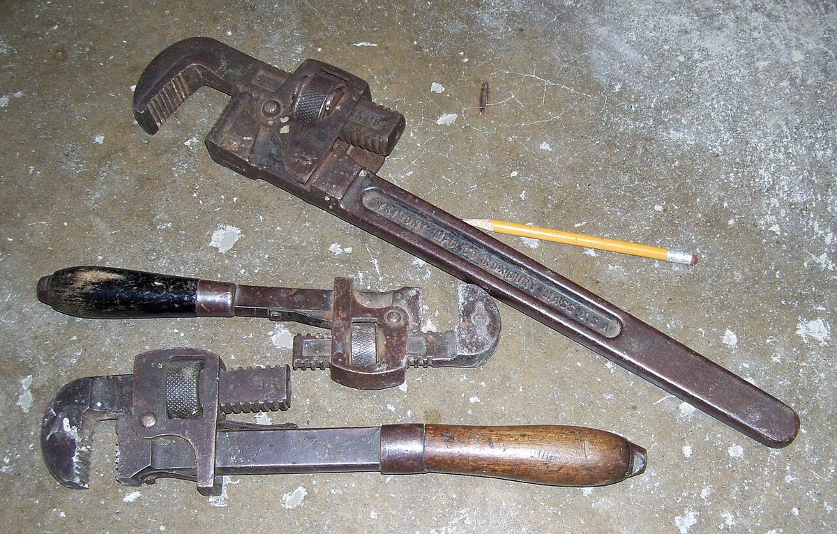 Three steel pipe wrenches lying on a concrete floor