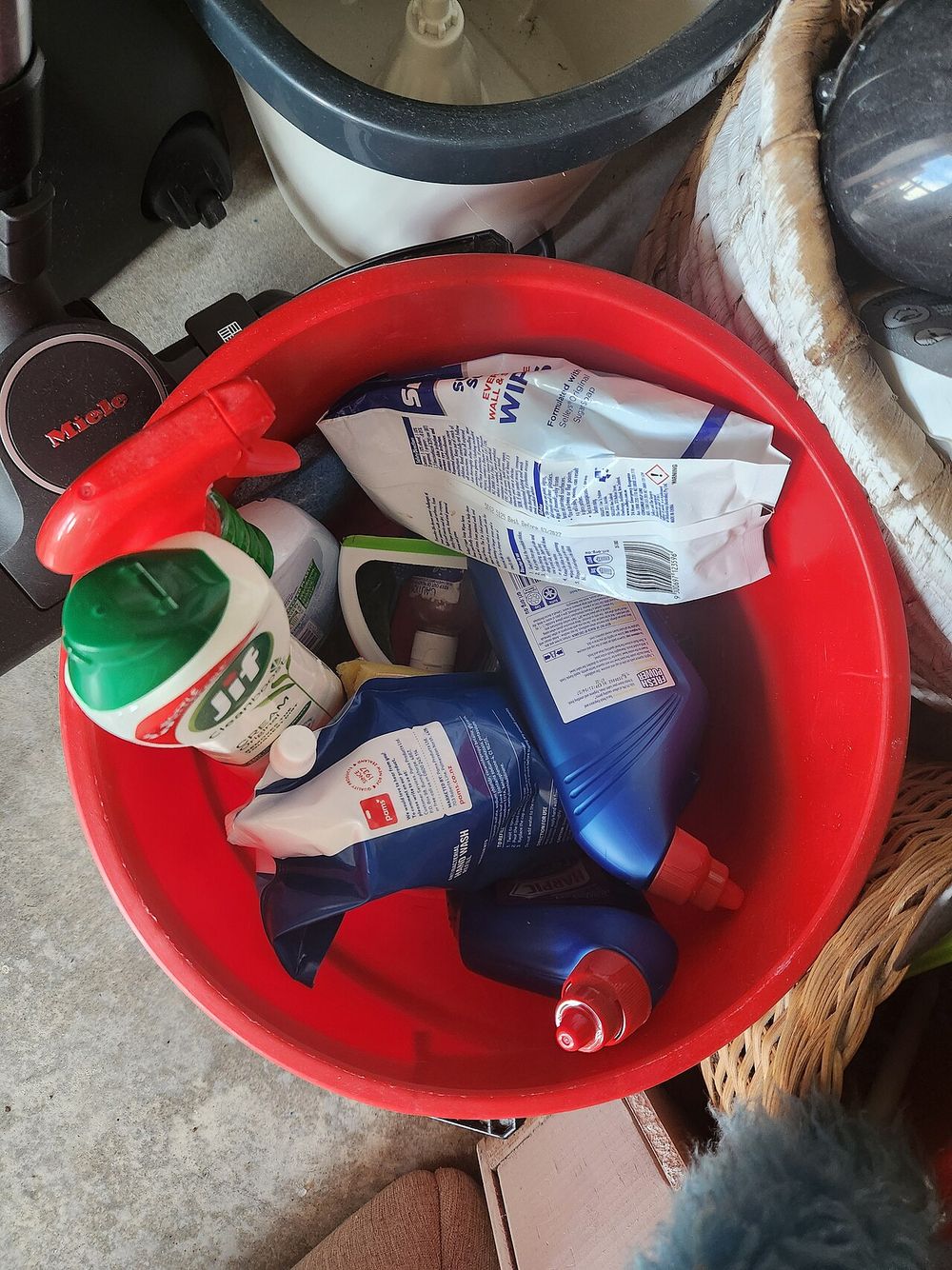A red bucket holding bottles of cleaning products and cloths