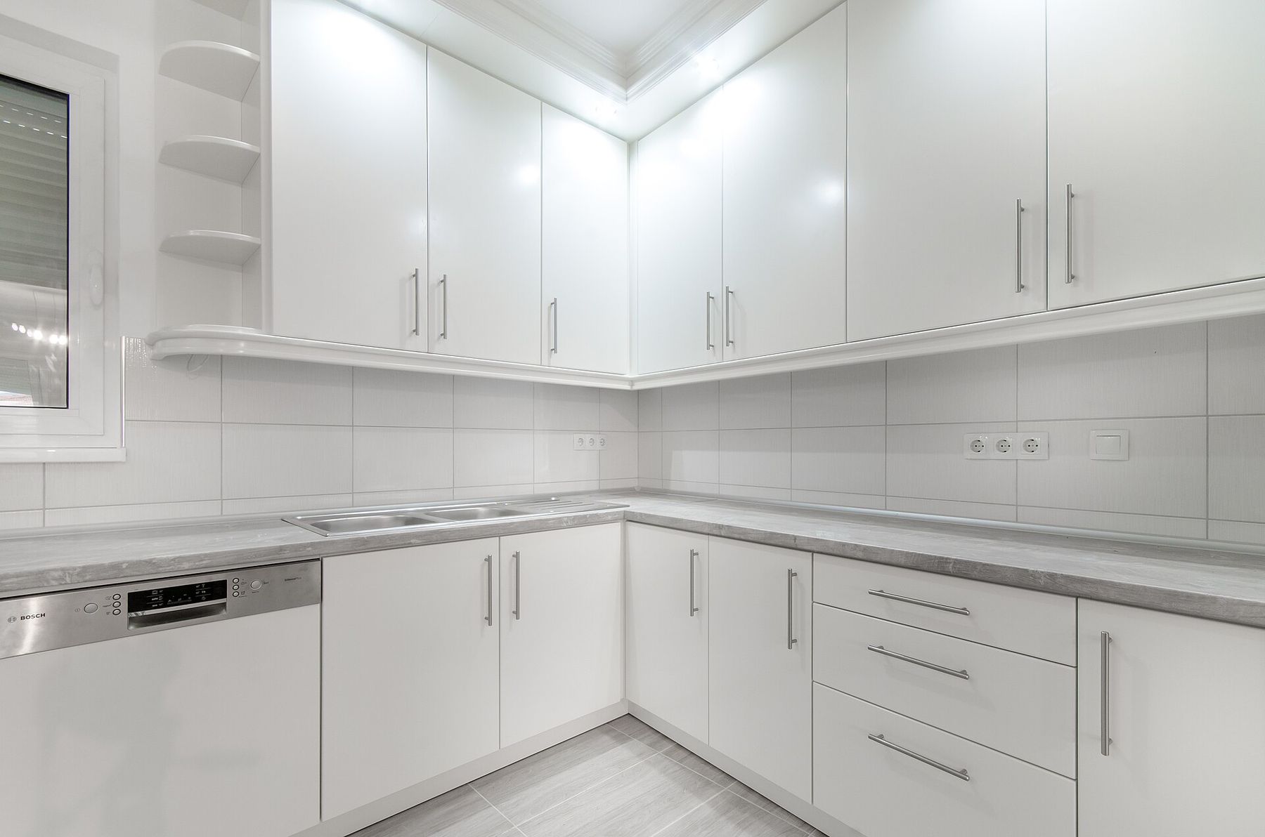A spotless white kitchen with glossy cabinets and a grey stone counter