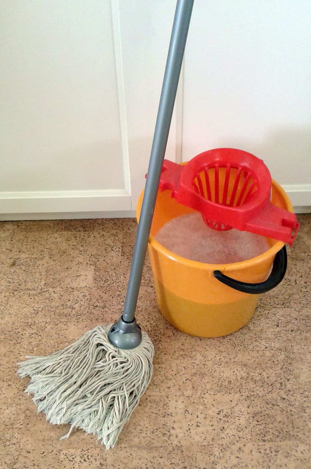 A string mop resting in a yellow bucket
