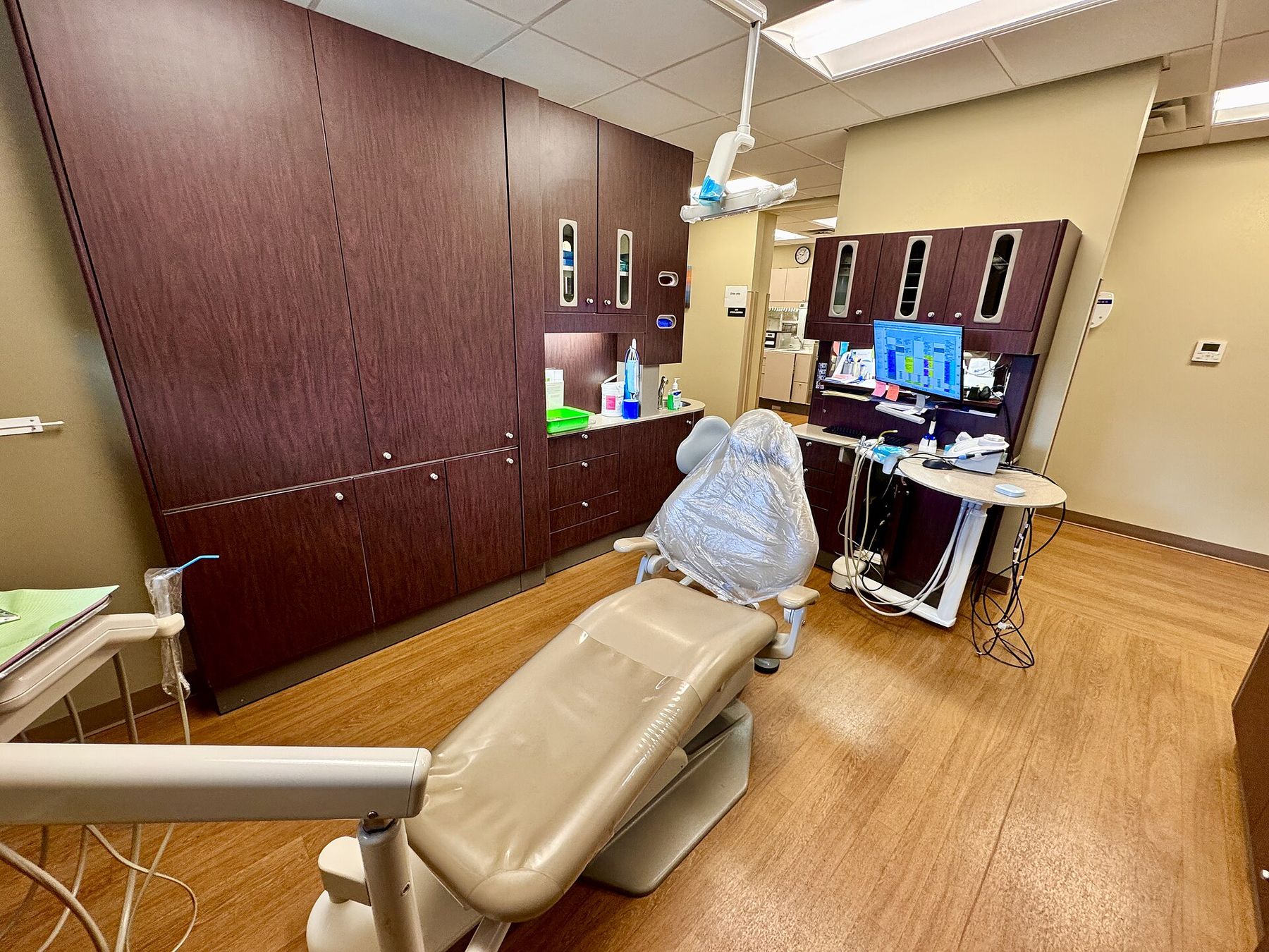 A dental treatment room with a reclining chair, wood cabinets and a monitor