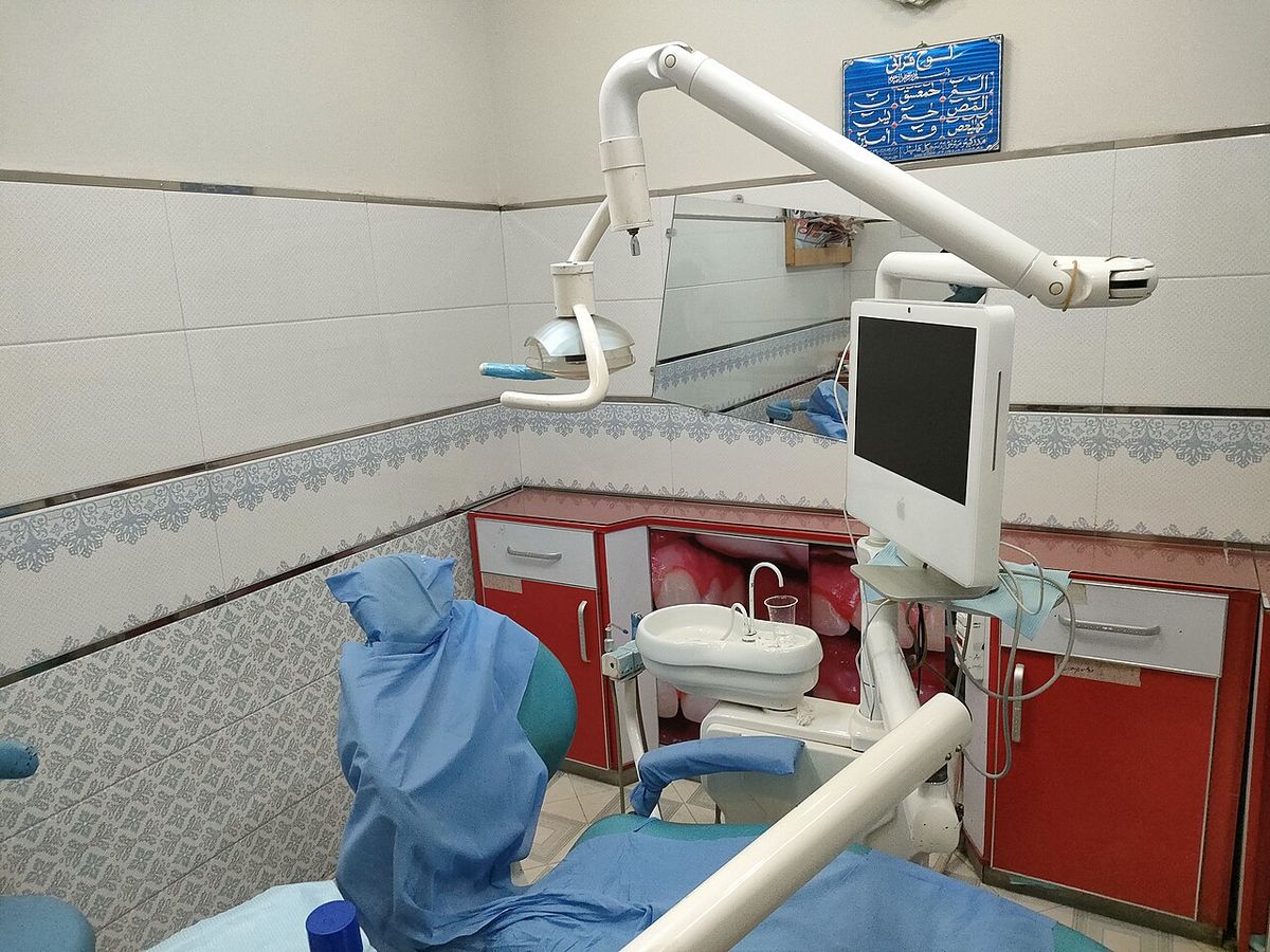 A dental chair with a light, a monitor and red cabinets