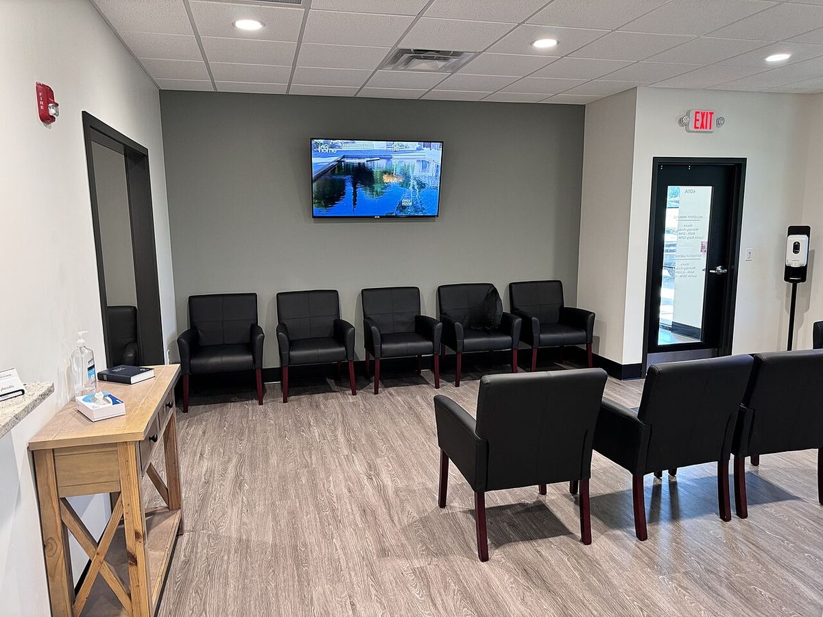 A quiet waiting room with black armchairs and a wall-mounted screen